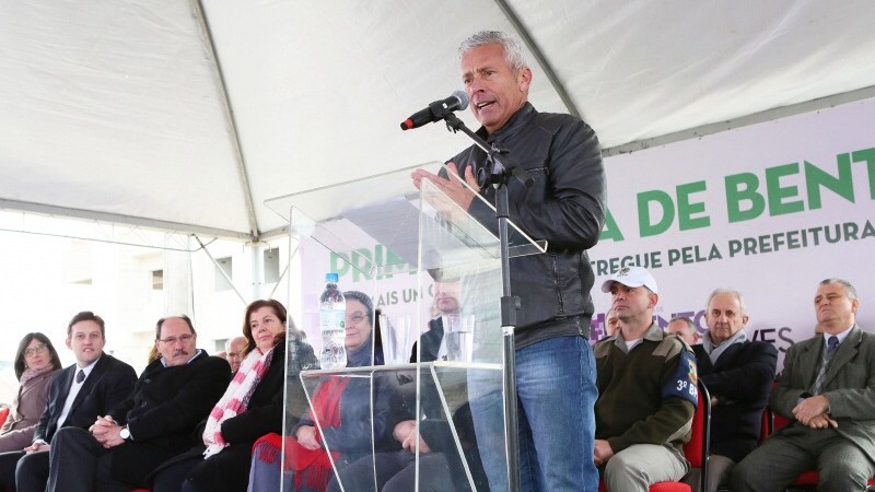 Atrás do púlpito com microfone, o Secretário Gabbardo discura. Algumas pessoas estão no palco sentadas, entre elas o Governador Sartori.