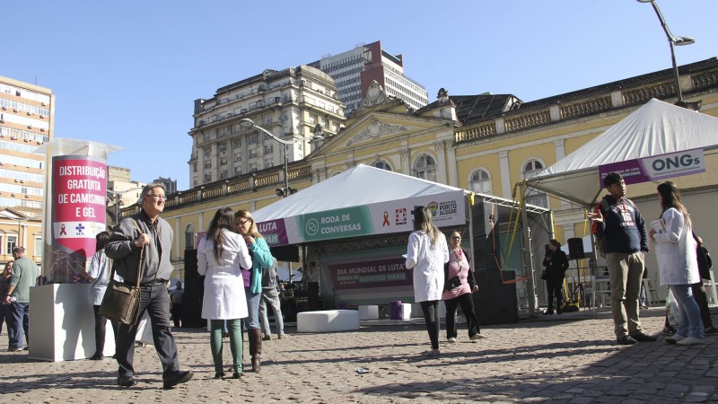 A imagem mostra o stand da Secretaria na frente do Mercado Público, em Porto Alegre. Na frente, algumas pessoas e profissionais de saúde.
