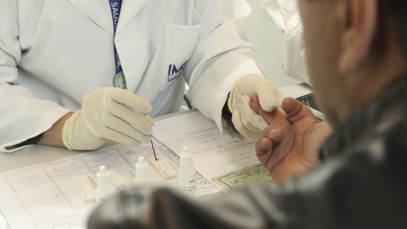 Profissional de saúde tira sangue do dedo de um homem e marca num papel.