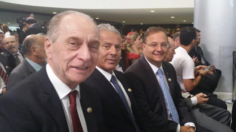Sentados no meio de várias pessoas, Lagreca; Gabbardo e Vila olham para a foto.