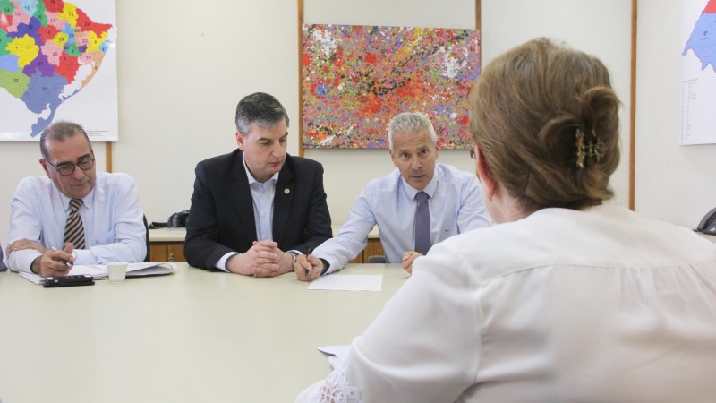 O Secret&aacute;rio Gabbardo, com um papel a sua frente, fala. Uma mulher a sua frente e dois homens, &agrave; sua esquerda, ouvem. Os quatro est&atilde;o sentados em volta de uma mesa. 