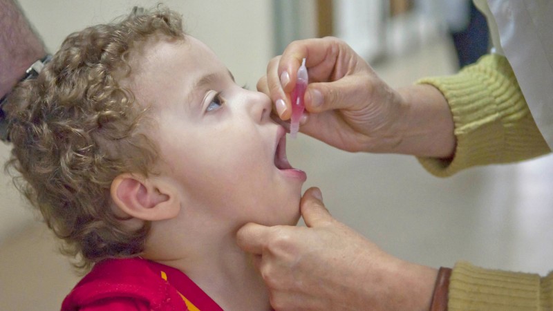 Uma profissional de saúde pinga gotas na boca de um menino. 