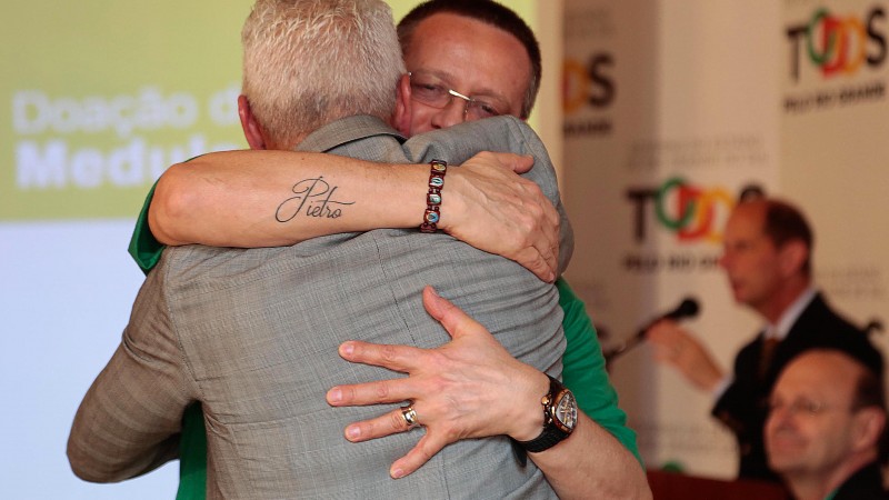 De costas, o Secretário Gabbardo abraça Beto Albuquerque, que mostra uma tatuagem escrita Pietro.