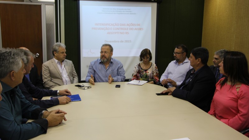 O Secretário Paz fala para alguns participantes da reunião (duas mulheres e sete homens). Todos estão sentados atrás de uma mesa redonda.