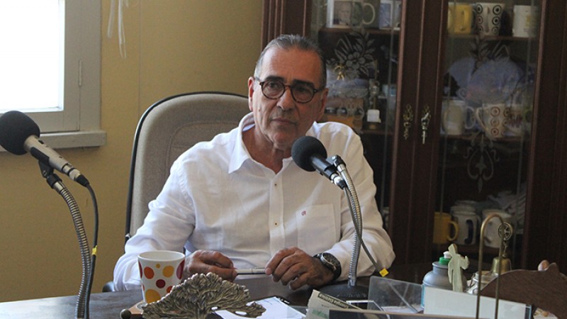 Sentado numa sala, Alexandre fala ao microfone.