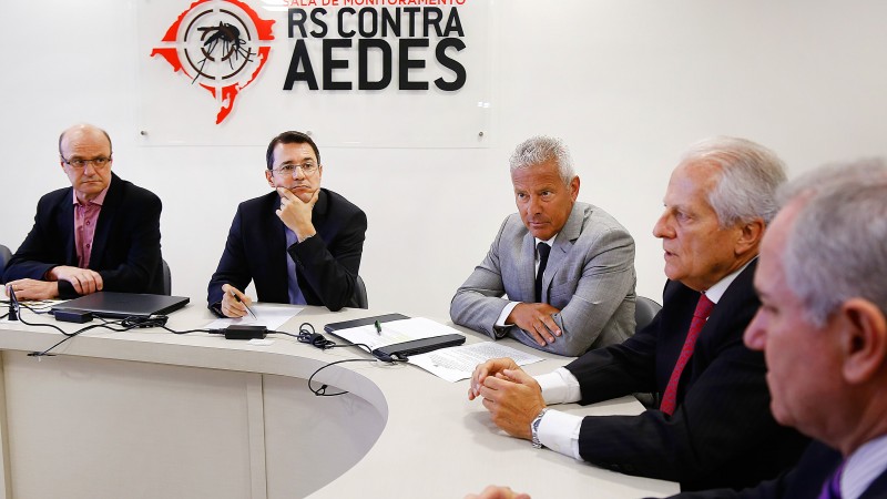 Cairoli fala, tendo ao seu lado o Secret&aacute;rio Gabbardo. Al&eacute;m deles, tr&ecirc;s homens. Todos est&atilde;o sentados atr&aacute;s de uma mesa circular. 