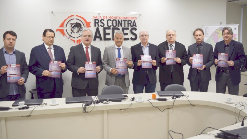De pé, atrás de uma mesa em formato de U, os Secretários Gabbardo e Westphalen e mais seis homens seguram panfletos.