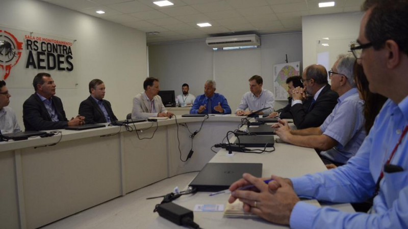 Um grupo de homens está sentado atrás de uma mesa em formato de U, entre eles o Secretário Gabbardo, que fala.