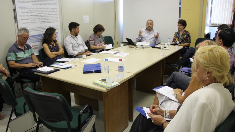 O Secretário Paz fala enquanto o grupo participante da reunião ouve. Todos estão sentados em volta de uma mesa.