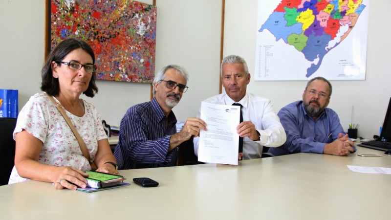 O Secretário Gabbardo e Roberto seguram um documento. Ana Maria e o Secretário Paz estão do lado. Os quatro estão sentados. 