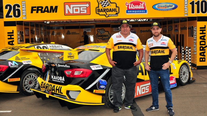 Os dois pilotos estão na frente dos carros e do box.