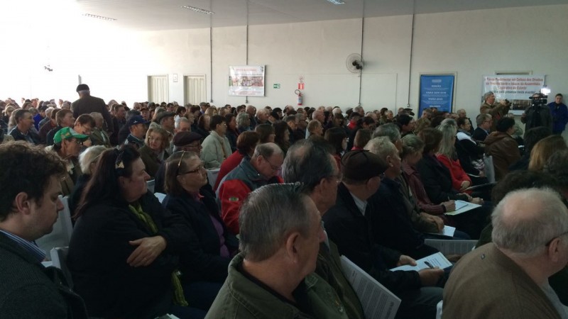 A imagem mostra um auditório lotado com a plateia sentada.