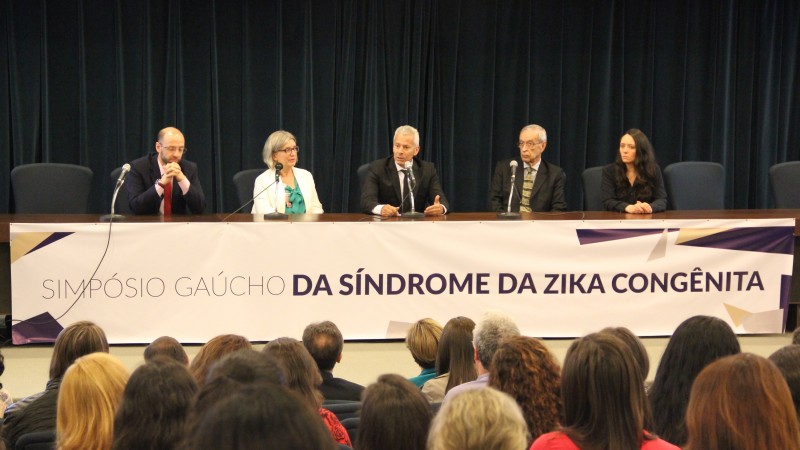 O Secretário Gabbardo fala. Ao lado dele, duas mulheres e dois homens. Os cinco estão sentados atrás de uma bancada.