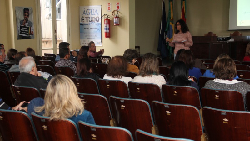 A palestrante fala de pé para uma plateia que assiste sentada.