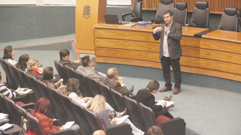 Juruena fala de pé segurando o microfone enquanto a plateia está sentada, ouvindo atenta.
