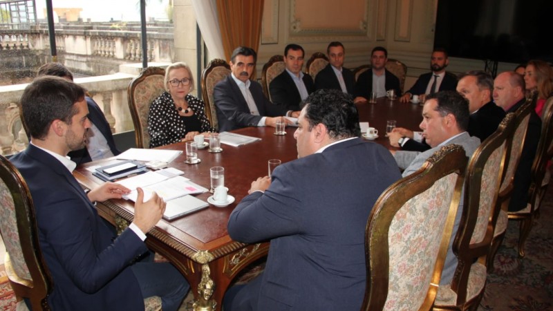 Reunião da equipe de Governo com várias pessoas sentadas a uma mesa entre elas o Governador Leite e a Secretária Arita.