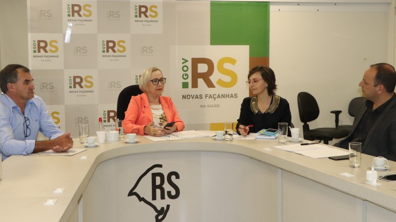 Quatro pessoas sentadas (entre elas, a Secretária Arita) em volta de uma mesa em formato de U. Atrás, vê-se o logotipo do Governo.