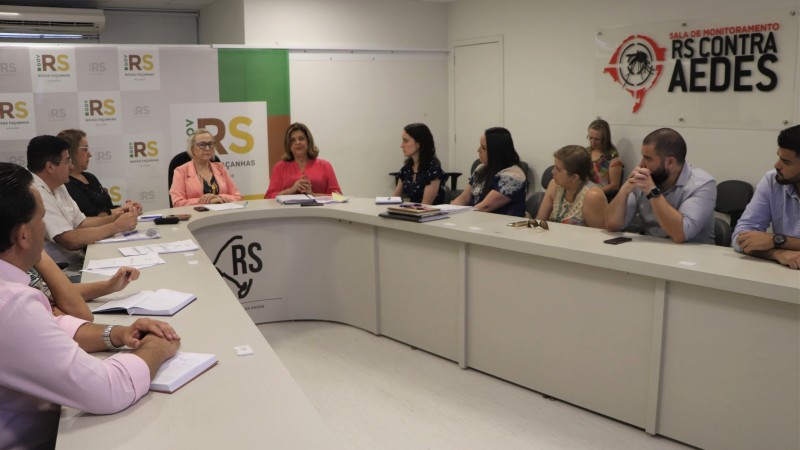 A imagem mostra várias pessoas sentadas atrás de uma em formato de U, entre elas as Secretárias Arita e Aglaé.  