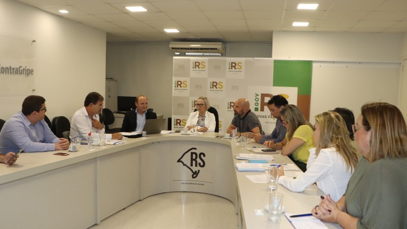Secretária Arita fala enquanto várias pessoas ouvem. Todos estão sentados atrás de uma mesa em formato de U.  