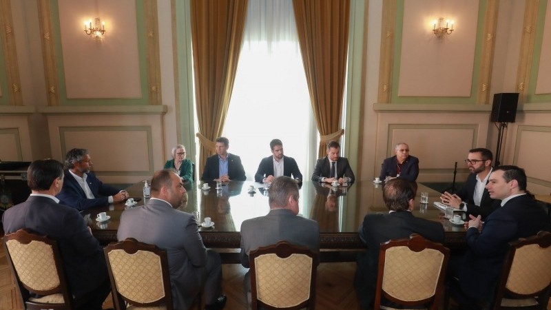A imagem mostra vários homens e a secretária Arita conversando em volta de uma mesa. 