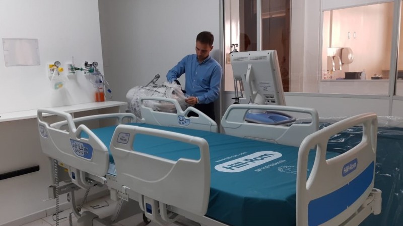 Hospital de Passo Fundo  UTI- um funcionário  abrindo um pacote em pé ao lado de uma cama hospitalar