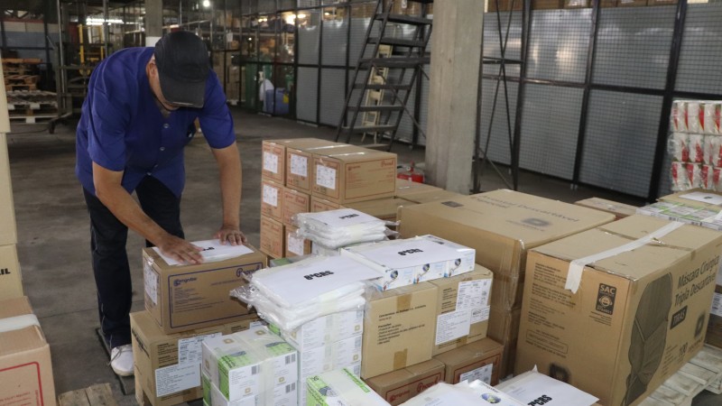 Num depósito, um funcionário mexe em uma caixa. Outras caixas estão ao redor. 
