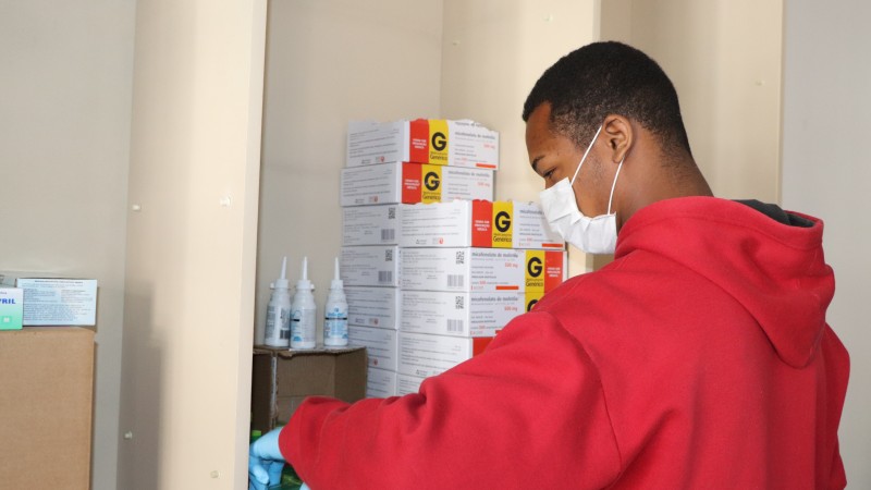 A imagem mostra um funcionário, de máscara, ajeitando caixas de remédios. 
