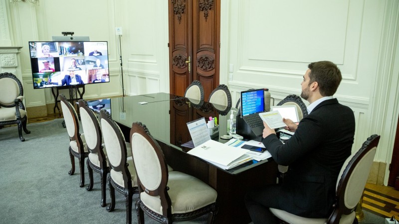 Governador Eduardo Leite assiste a videoconferência que passa no telão a sua frente. 