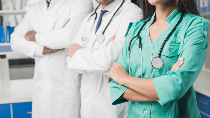 A imagem mostra três profissionais de saúde, dois homens e uma mulher. 