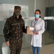 Um militar e uma profissional de saúde seguram uma caixa. Os dois estão de máscara. 