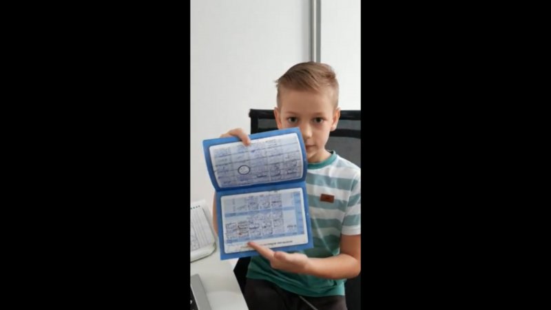 A imagem mostra um menino loiro segurando a sua carteira de vacinação aberta.