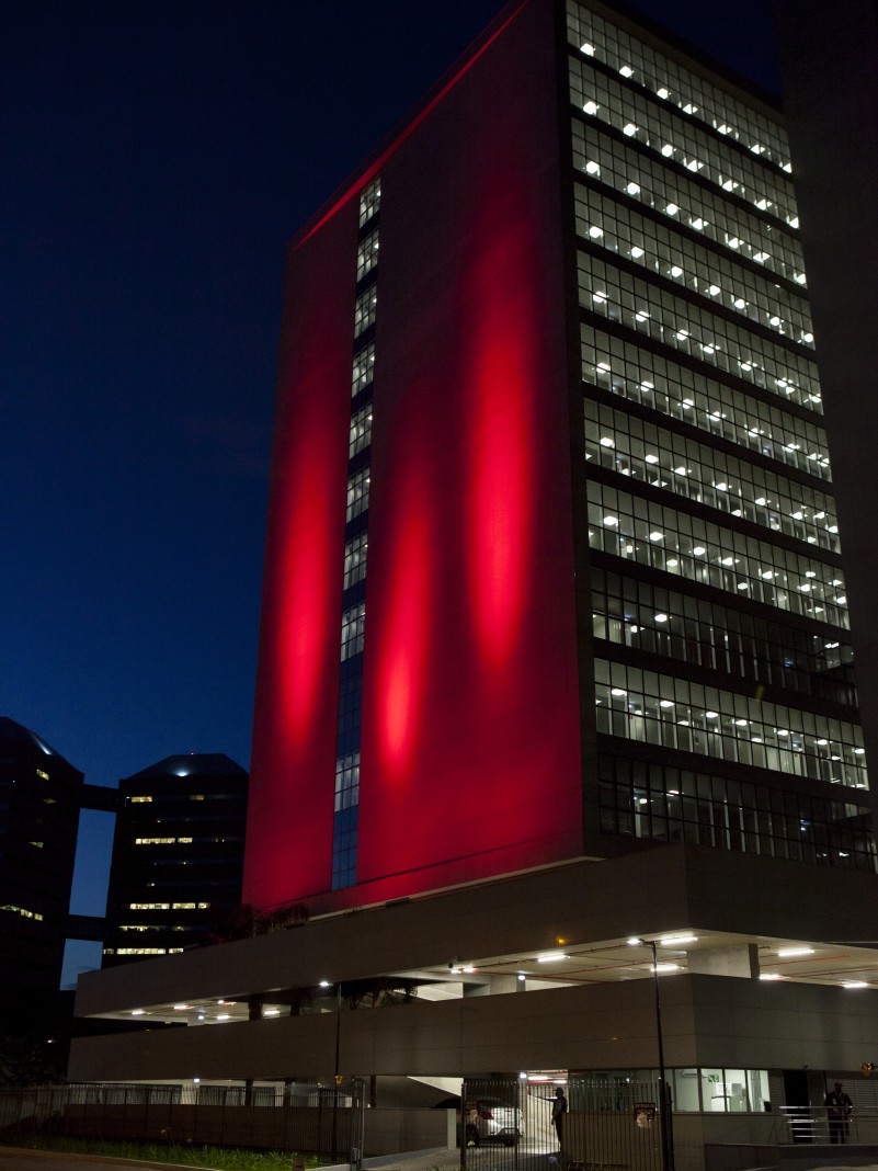 A imagem mostra o prédio da Tribunal de Justiça do Rio Grande do Sul iluminado de vermelho. A foto foi tirada de noite. 