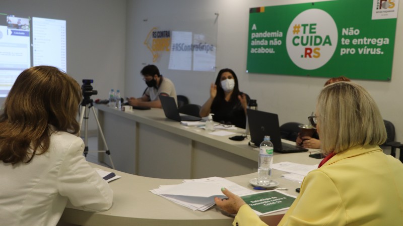 A Secretária Arita ouve uma das participantes da reunião. Todos estão sentados atrás de uma mesa que tem o formato de U. 