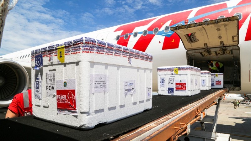 A imagem mostra um lote de vacinas entrando no avião.