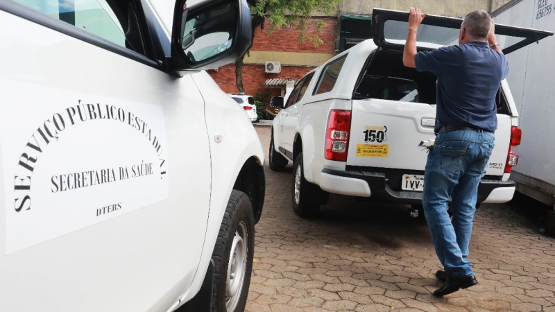 A imagem mostra um homem abrindo a parte de trás de uma caminhonete. Do lado, tem um carro. 