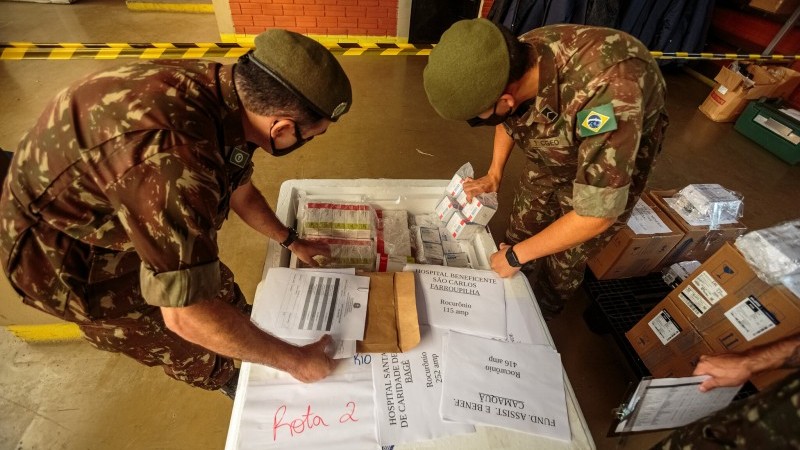 Dois militares verificam caixas de vacinas que estão dentro de uma caixa. 