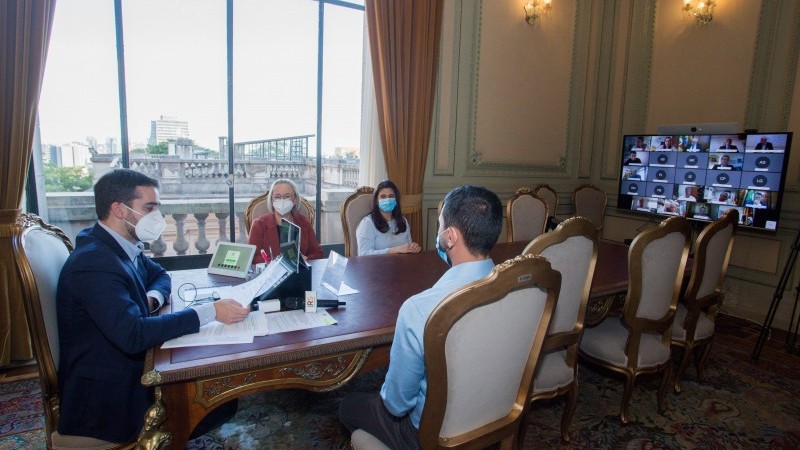 Governador Eduardo Leite, secretária Arita e mais dois diretores da SES participam de videoconferência. Todos estão de máscaras e sentados atrás de uma mesa.  