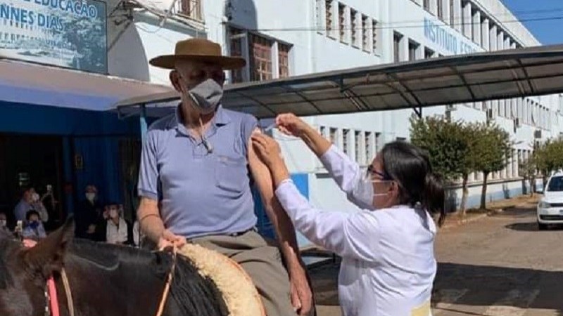 Homem sendo vacinado por uma profissional de saúde montado em um cavalo em Cruz Alta. Os dois estão de máscara. 