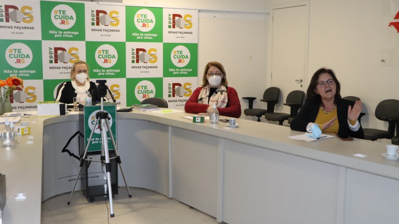 Secretária e duas especialistas em saúde participam da live na sala de monitoramento. Uma especialista está falando.