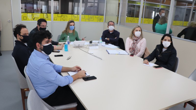 Reunião com sete pessoas (quatro homens e três mulheres) em volta de uma mesa de trabalho. Todos estão de máscara.
