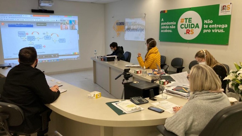 Secretária Arita e mais quatro participantes da reunião acompanham as informações que está no telão projetado à frente.