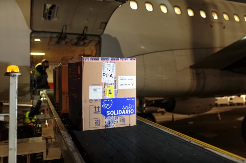 A imagem mostra caixas grandes com doses da vacina na esteira que vem do avião. Foto noturna.