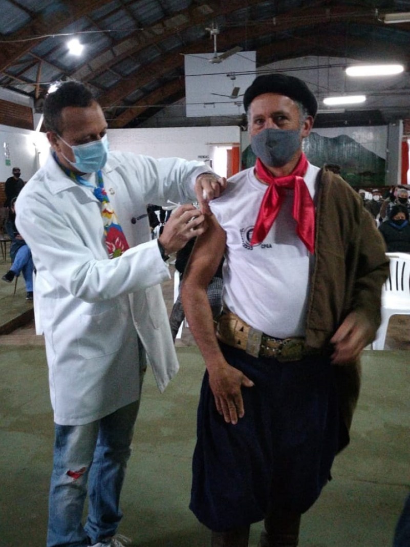 Um profissional de saúde vacina um homem vestido de gaúcho. 