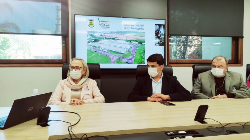 Secretaria Arita e mais dois homens, sentados e de máscara, olham para o lado.