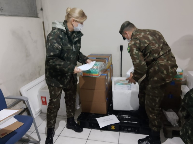 Dois militares (uma mulher e um homem) fazem a conferência de caixas e frascos num depósito.