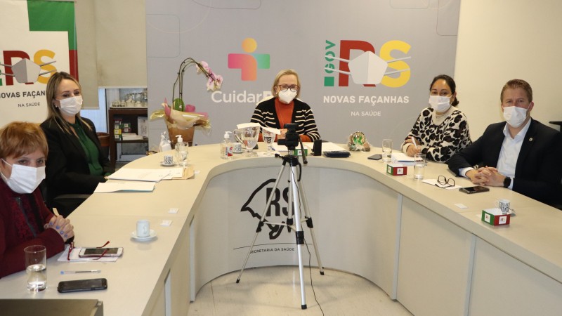 Secretária Arita e mais quatro pessoas (três mulheres e um homem) olham para a frente. Todos estão de máscara e sentados atrás de uma mesa.
