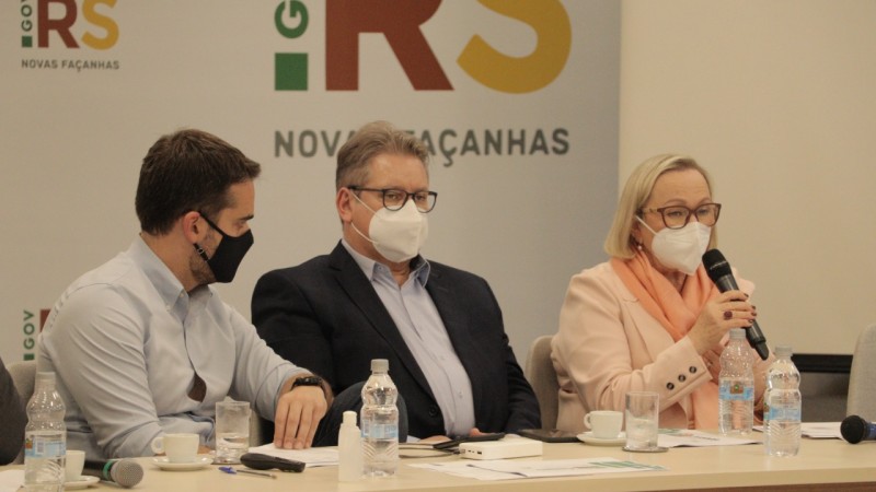 A secretária Arita Bergmann fala na reunião ao lado do governador Eduardo Leite e do vice-governador Ranolfo Vieira Júnior. Os três estão sentados e de máscara.
