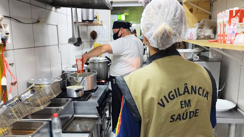 Uma profissional da Vigilância em Saúde observa um profissional cozinhando.