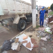Funcionário, de pé e ao lado de um caminhão, observa lixo jogado no chão.