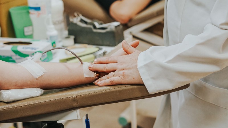 A imagem mostra a mão de uma profissional segurando o braço de uma pessoa que faz a doação de sangue. 
